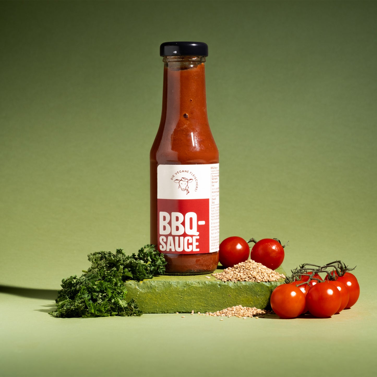 Vegane BBQ-Sauce in Glasflasche mit frischen Tomaten, Petersilie und Körnern auf grünem Podest, 100% pflanzlich