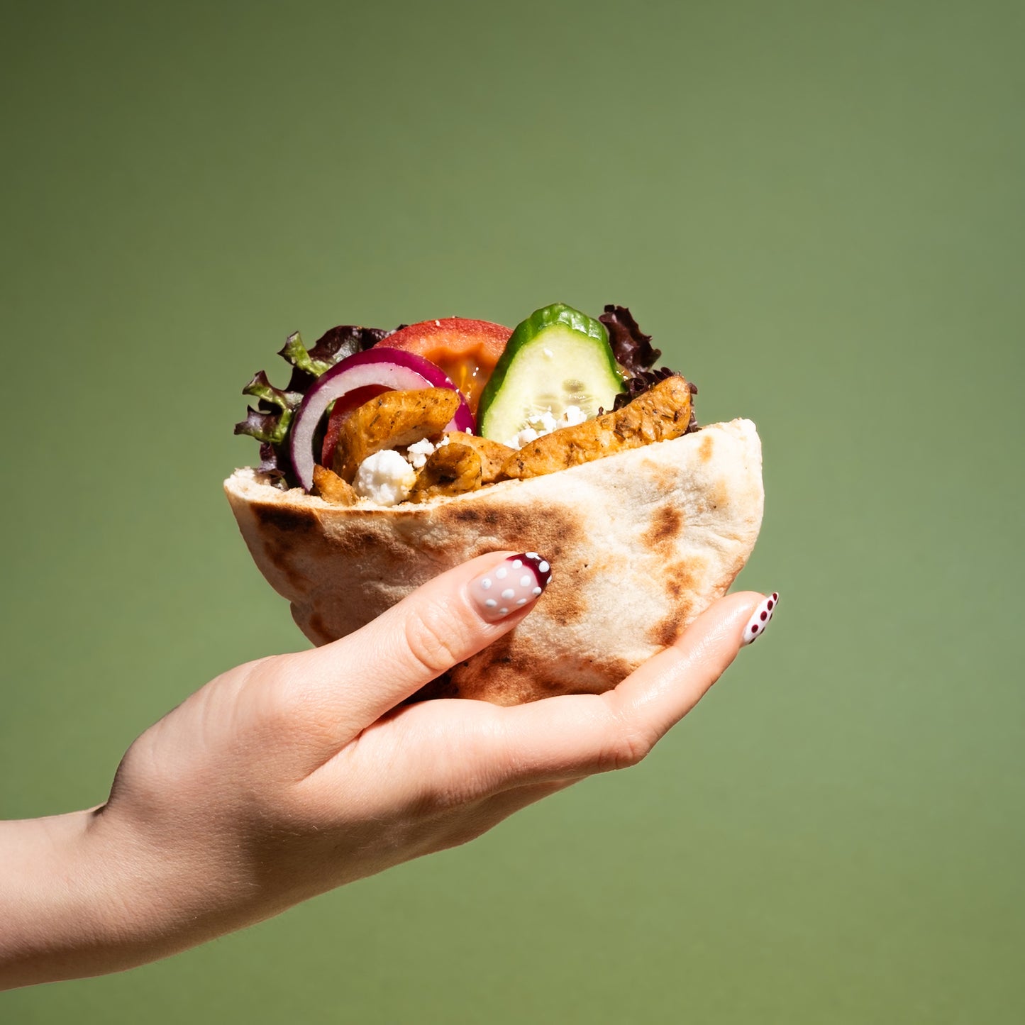 Hand hält pflanzlichen Gyro mit veganem Hähnchen, Salat, Gurke, Zwiebel und Feta in Fladenbrot – proteinreich & 100% vegan