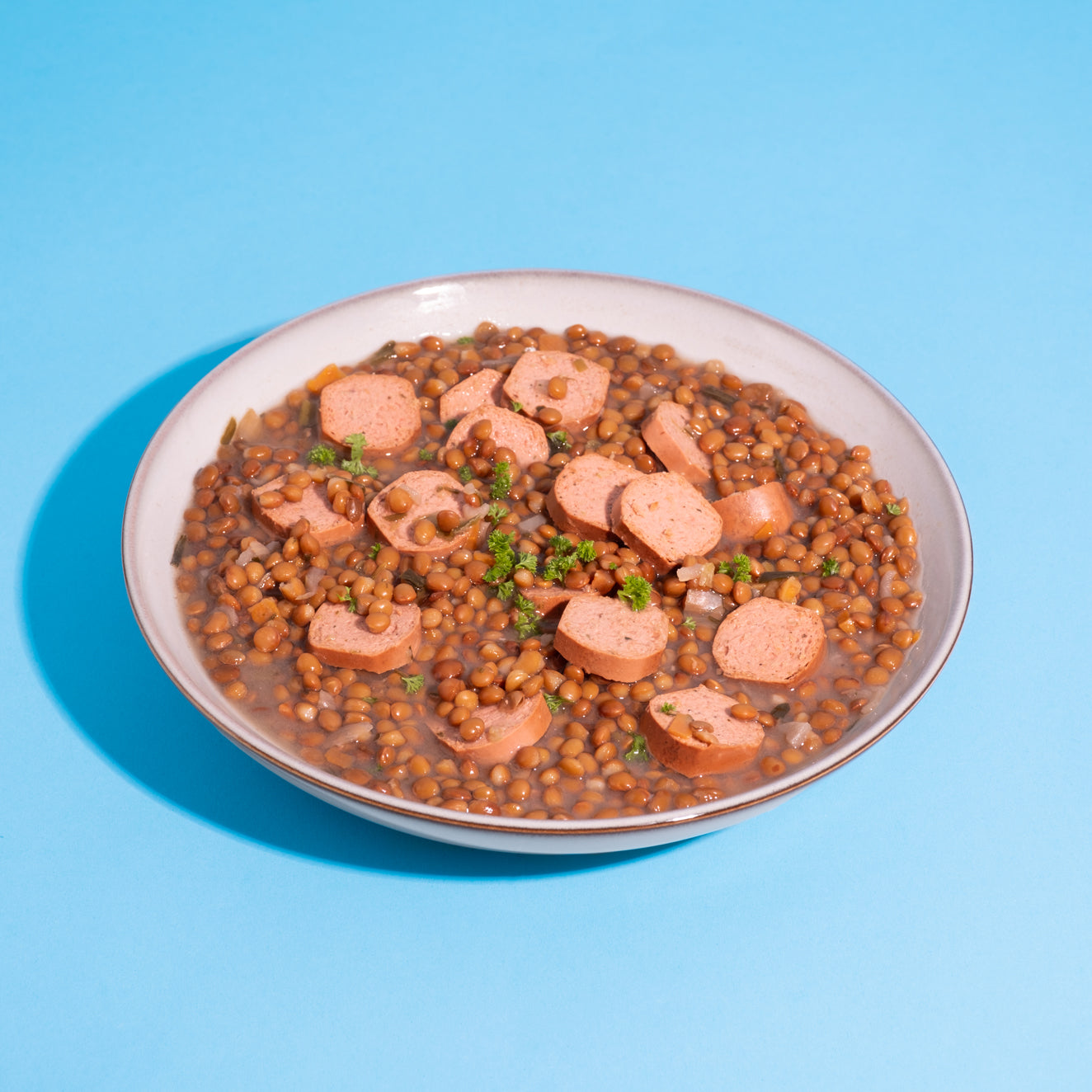 Vegane Kochmettwurst in Linsengericht vor blauem Hintergrund.