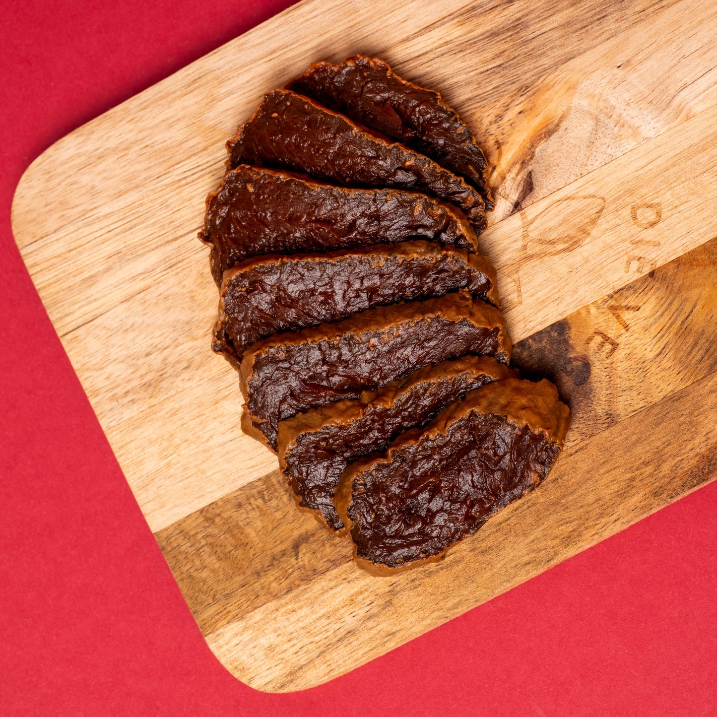 Mehrere dünne Scheiben dunkelroter Rote-Bete-Schinken auf hellem Holzbrett, roter Hintergrund.