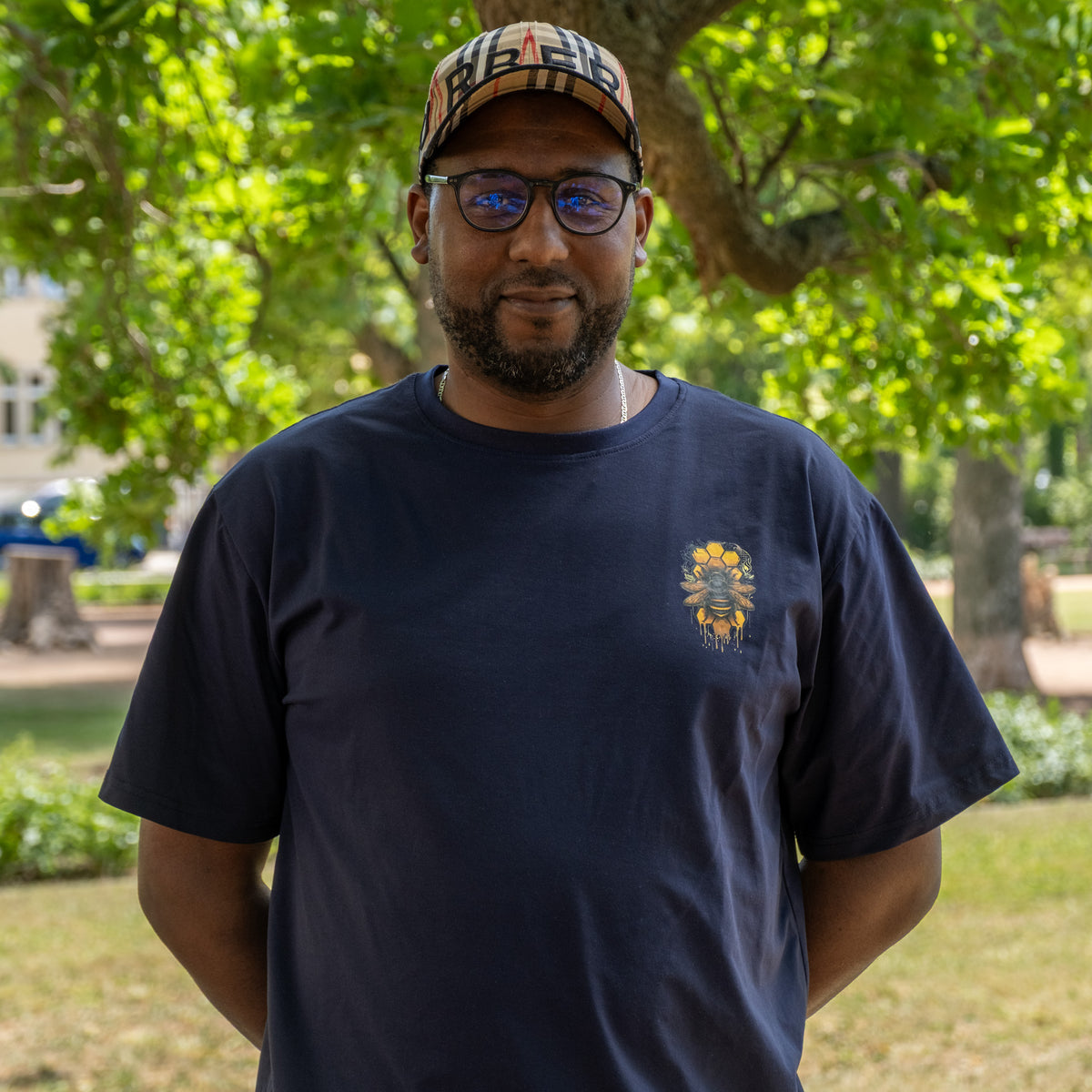Abdul aus der Produktion, im Park mit Kappe, Brille und dunkelblauem T-Shirt
