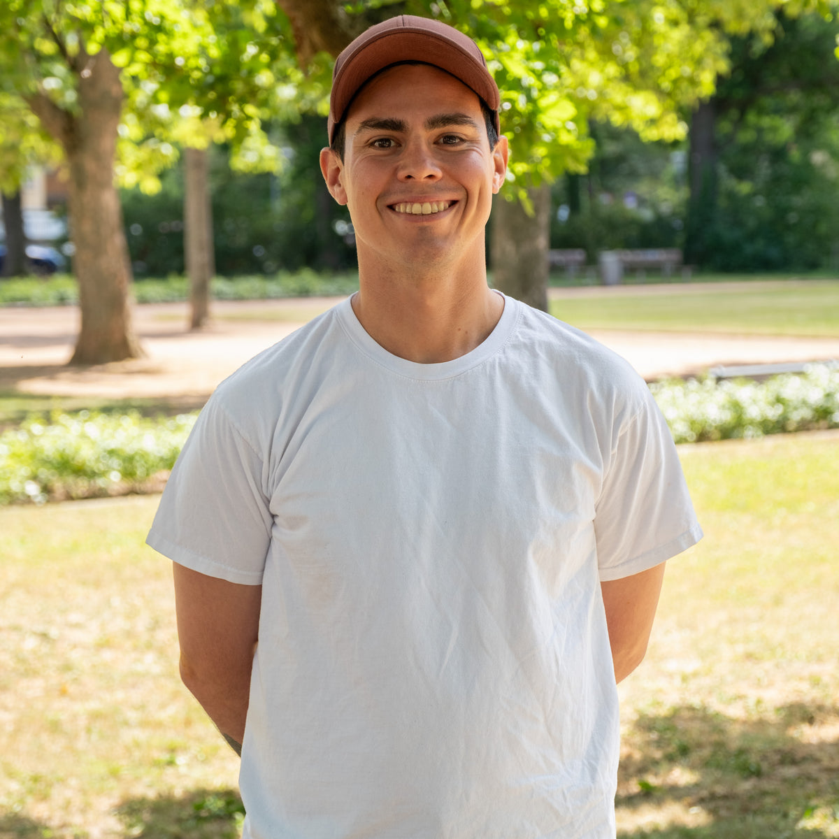 Alfonso aus der Produktion, lächelnd im Park, mit roter Kappe und weißem T-Shirt