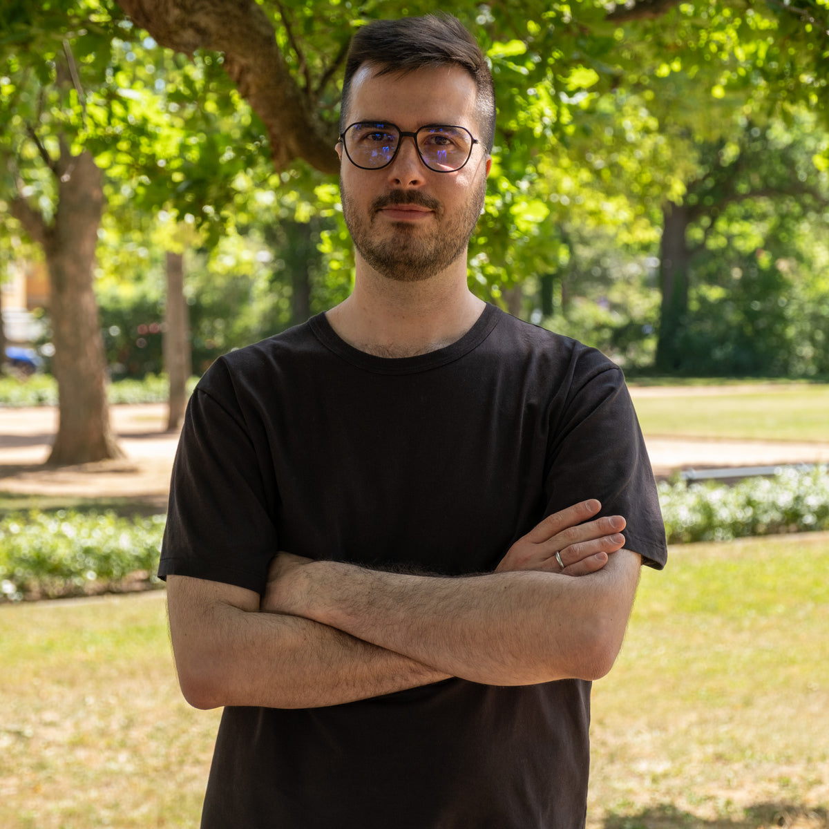 Axel, Leitung Performance Marketing & Fulfillment, mit verschränkten Armen im Park, Brille und schwarzem T-Shirt