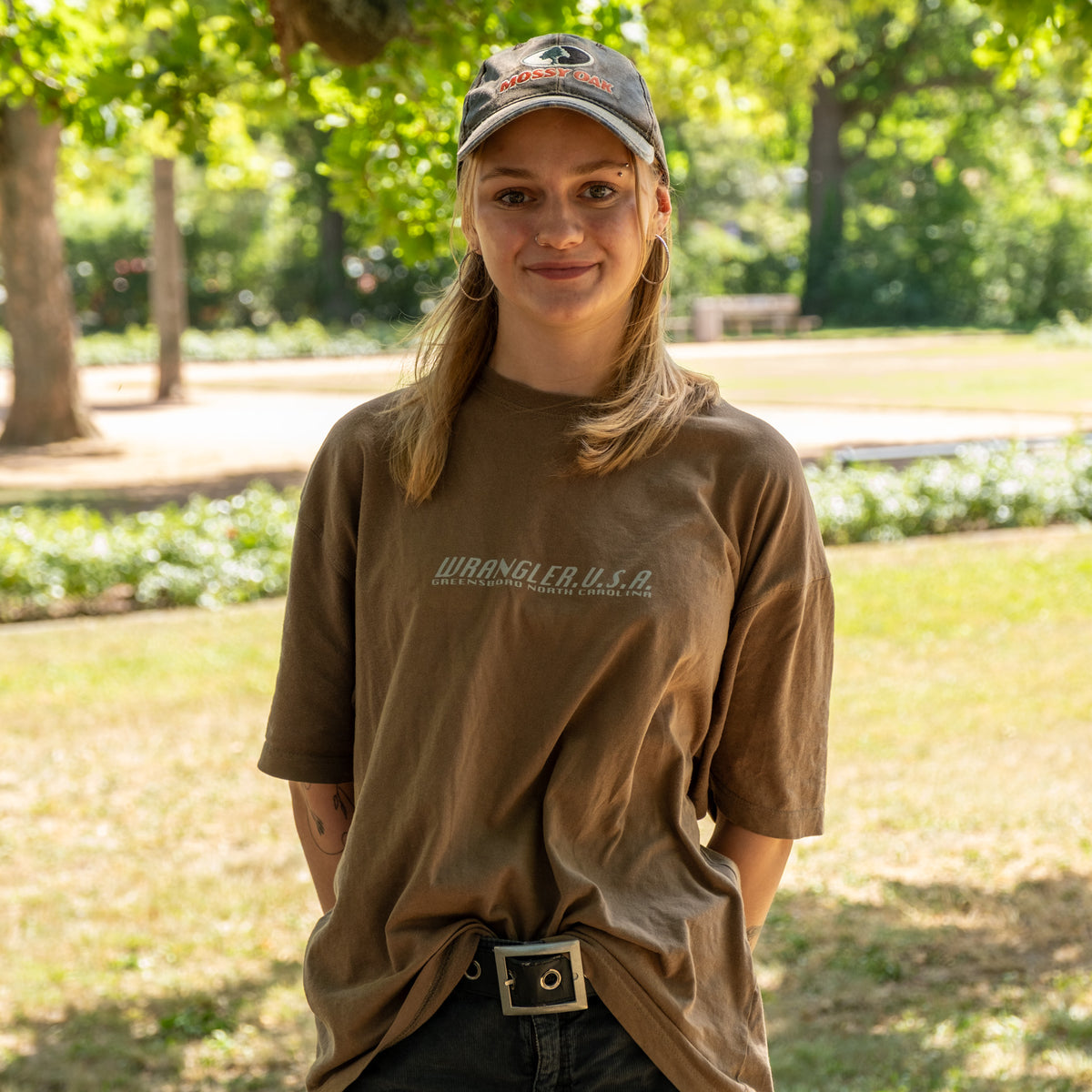 Mia aus dem Team der Veganen Fleischerei, lächelnd im Park mit Kappe und braunem T-Shirt