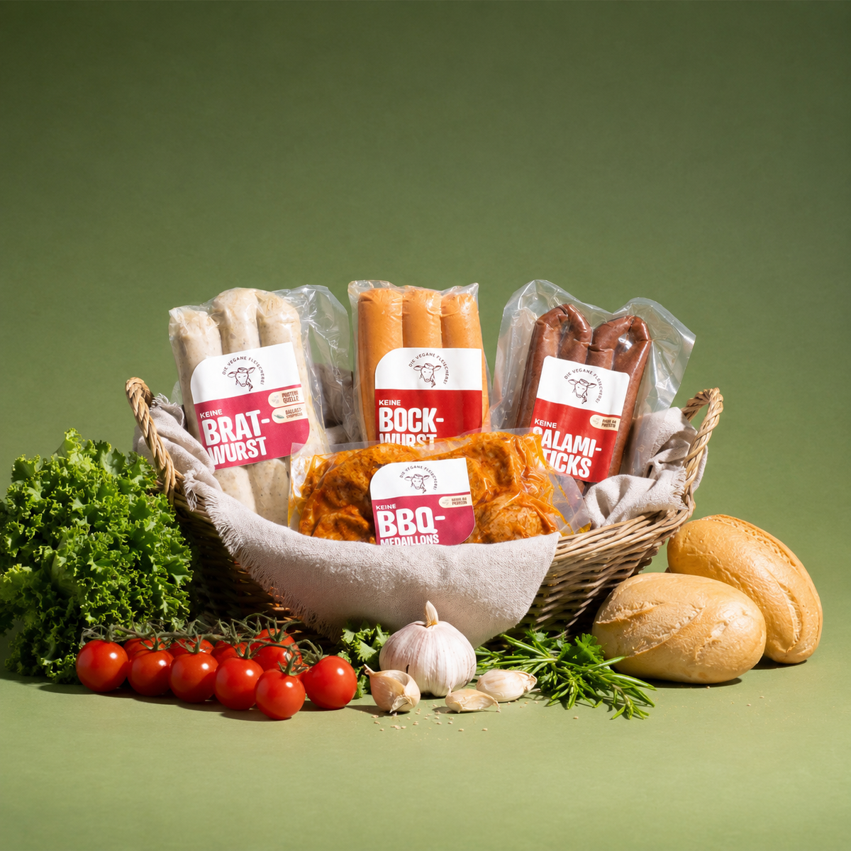 Weidenkorb mit „Keine Bratwurst“, „Keine Bockwurst“, „Keine Salami-Sticks“ und „Keine BBQ-Medaillons“, daneben Salat, Tomaten, Knoblauch und Brötchen