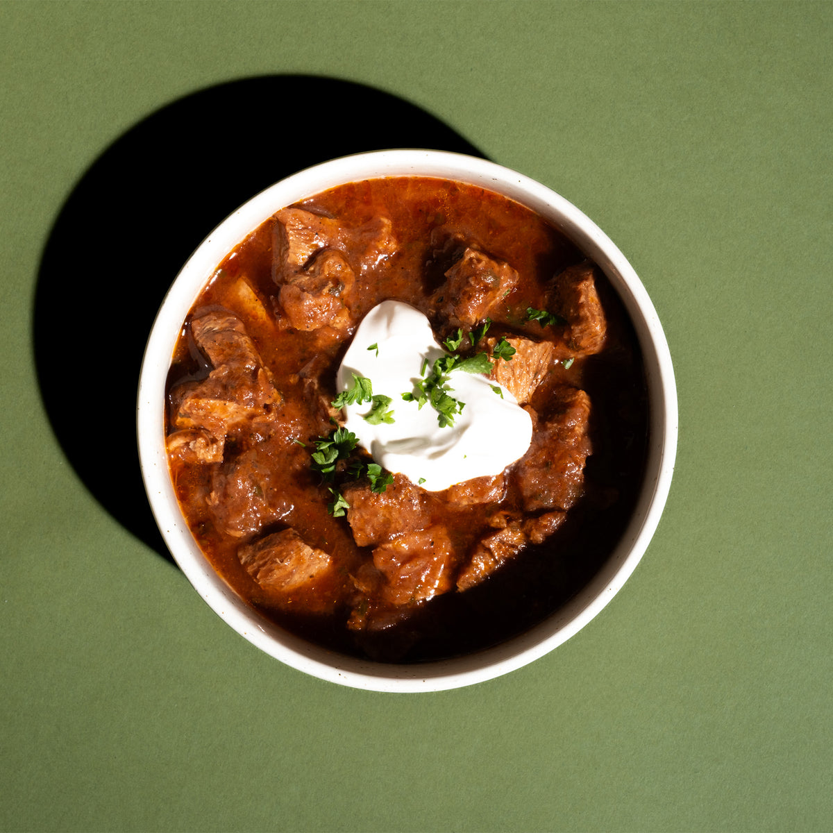 „Kein Schwarzbiergulasch“ mit einem Klecks heller Creme und Petersilie in einer Schale, von oben fotografiert