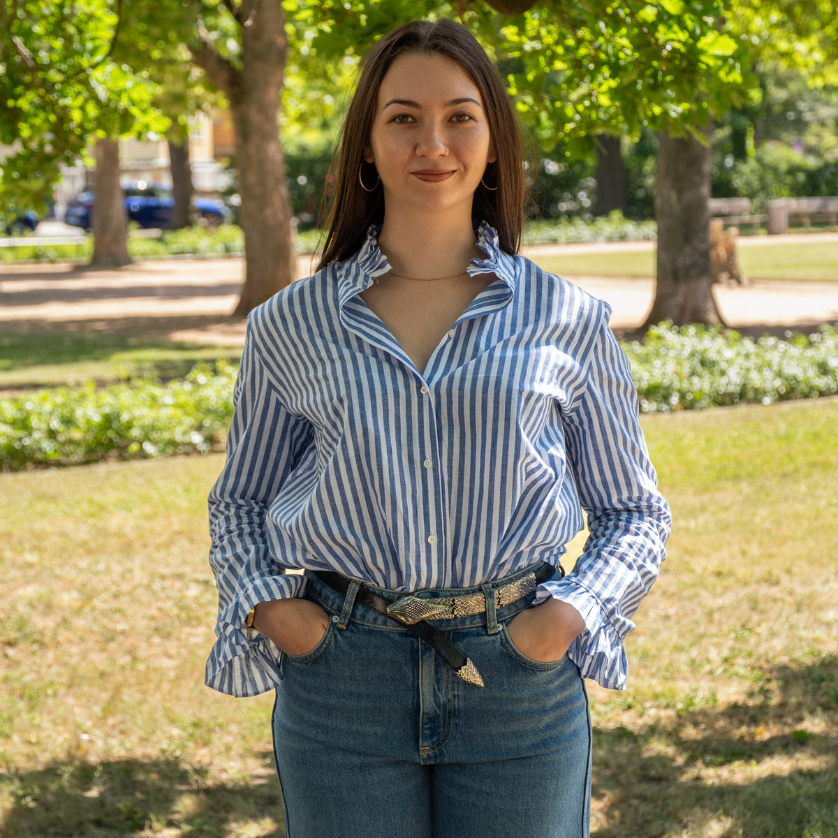 Shirley, Prokuristin und Leitung Marketing, im Park in blau-weiß gestreifter Bluse und Jeans