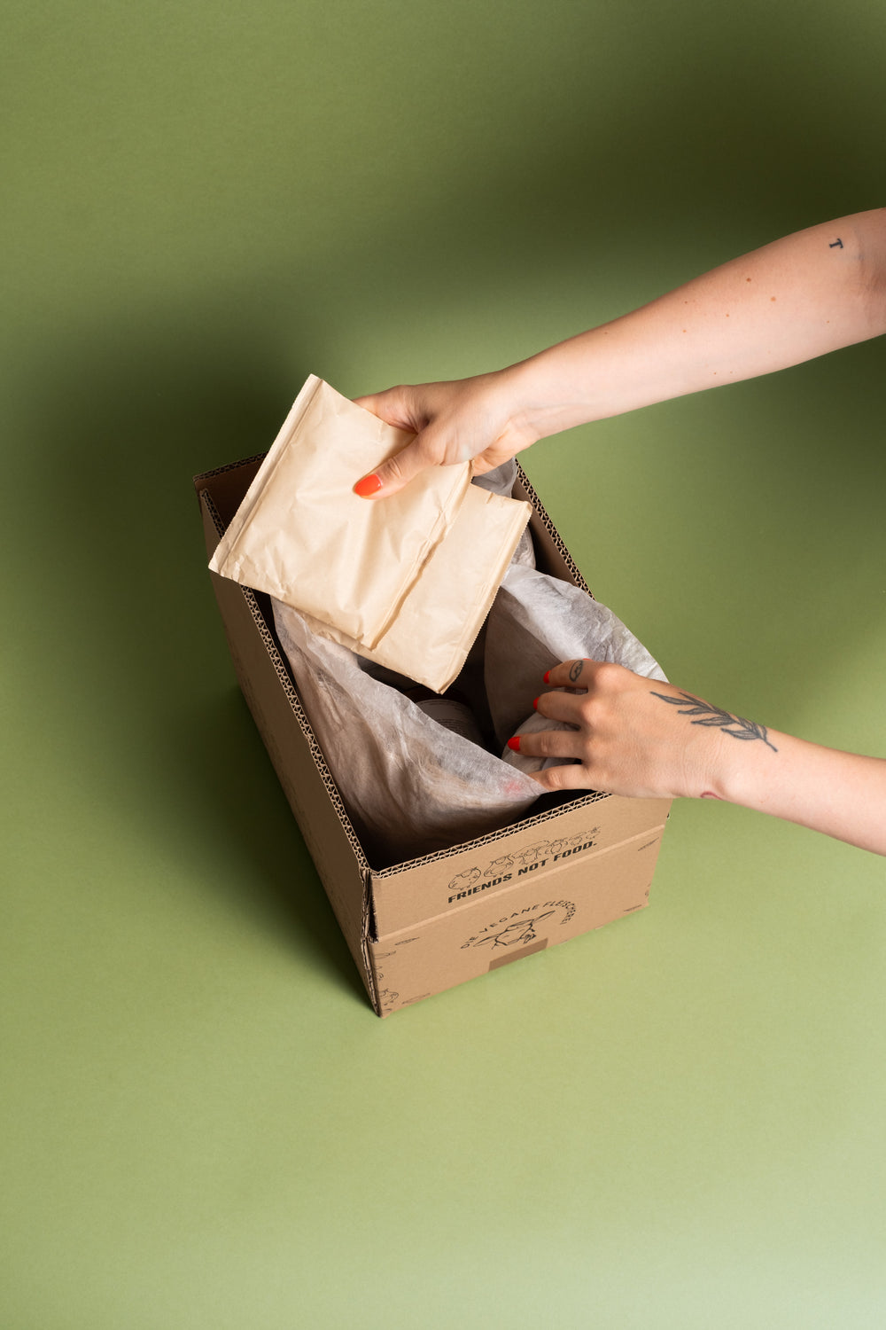 Hände legen einen Kühlakku in Papierhülle in den Versandkarton mit „Friends not Food“-Aufdruck