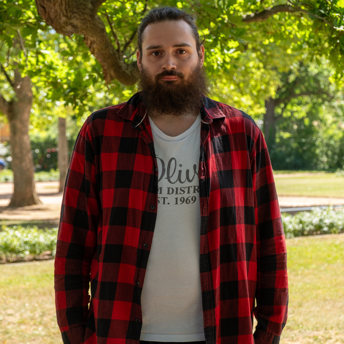 Domenik aus der Produktion, im Park mit Vollbart und rot-schwarz kariertem Hemd