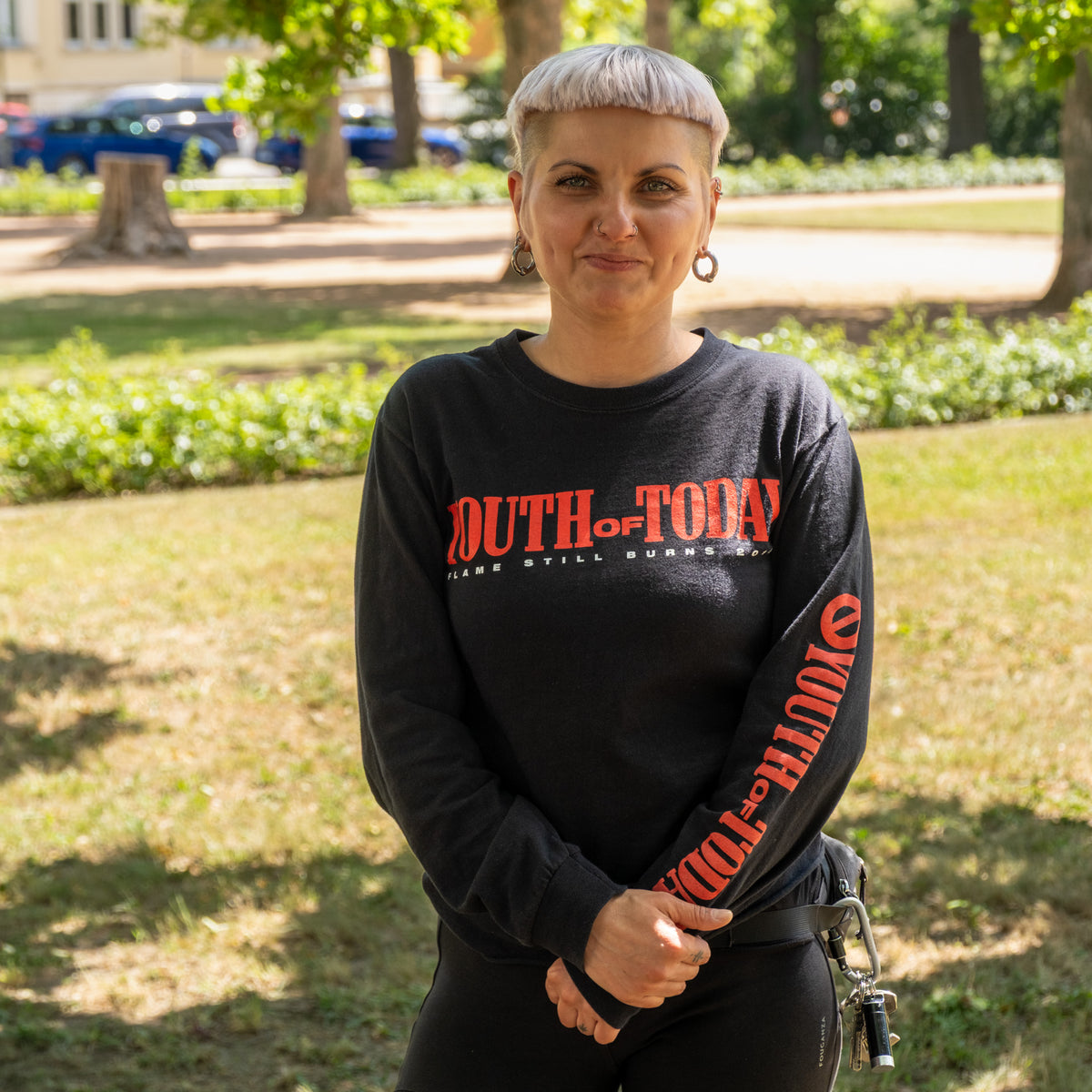 Kate aus der Logistik, im Park mit hellblonden kurzen Haaren und schwarzem Pullover
