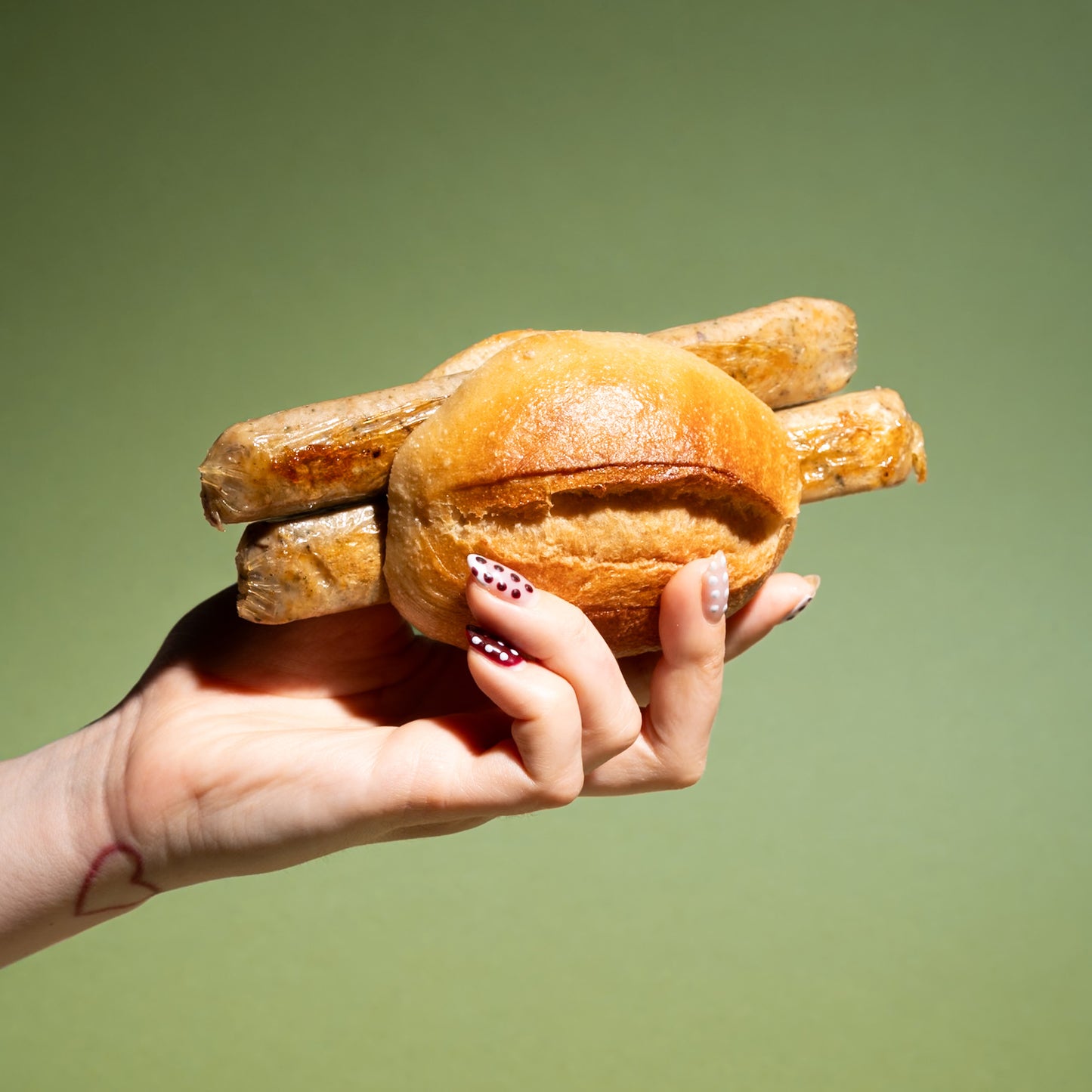 Hand hält Brötchen mit drei veganen Bratwürsten, proteinreich und 100% pflanzlich, grüner Hintergrund