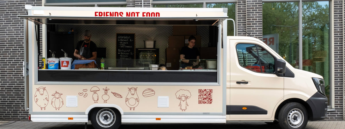 Foodtruck der Veganen Fleischerei mit Schriftzug „Friends not Food“ und geöffneter Verkaufsklappe, zwei Mitarbeitende im Inneren