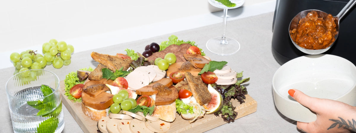 Catering-Platte mit veganem Aufschnitt und Brot auf Holzbrett, daneben wird Gulasch aus einem Warmhaltebehälter geschöpft