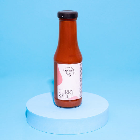 Flasche Curry-Sauce auf blauem Podest vor blauem Hintergrund.