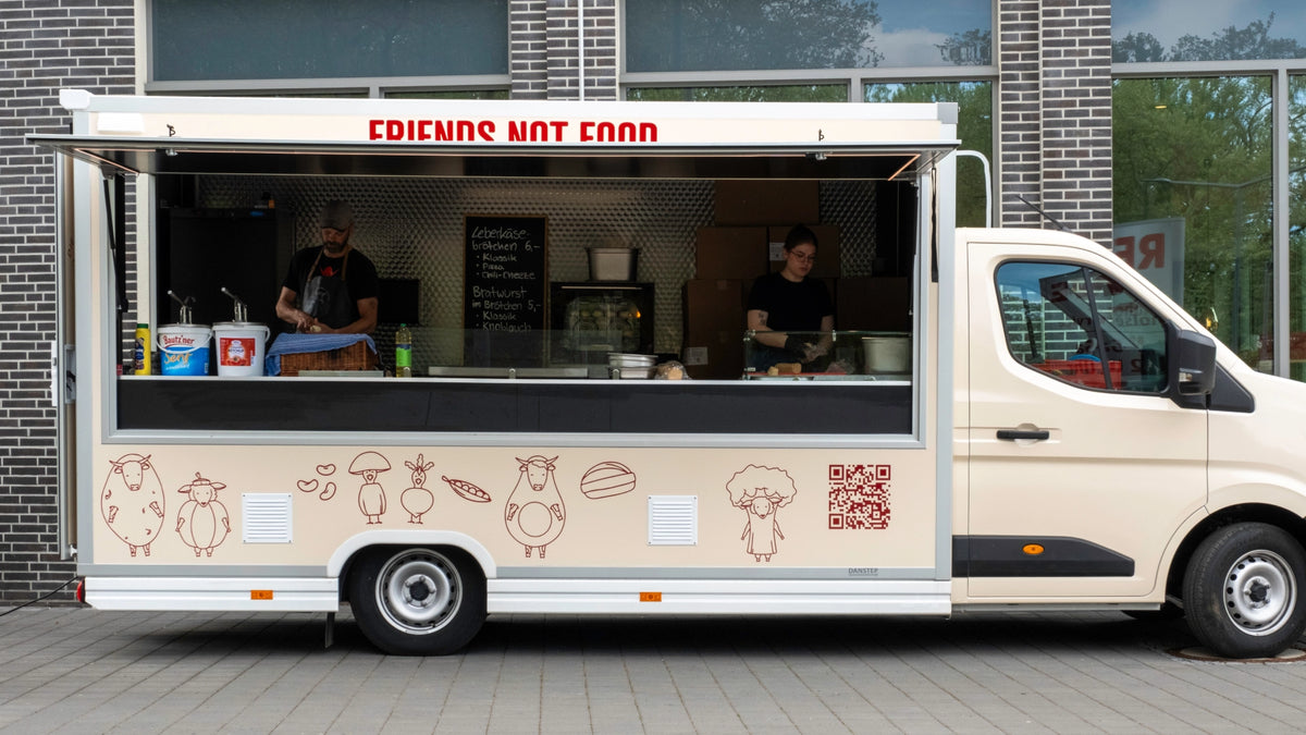 Foodtruck der Veganen Fleischerei mit Schriftzug „Friends not Food“ und geöffneter Verkaufsklappe, zwei Mitarbeitende im Inneren