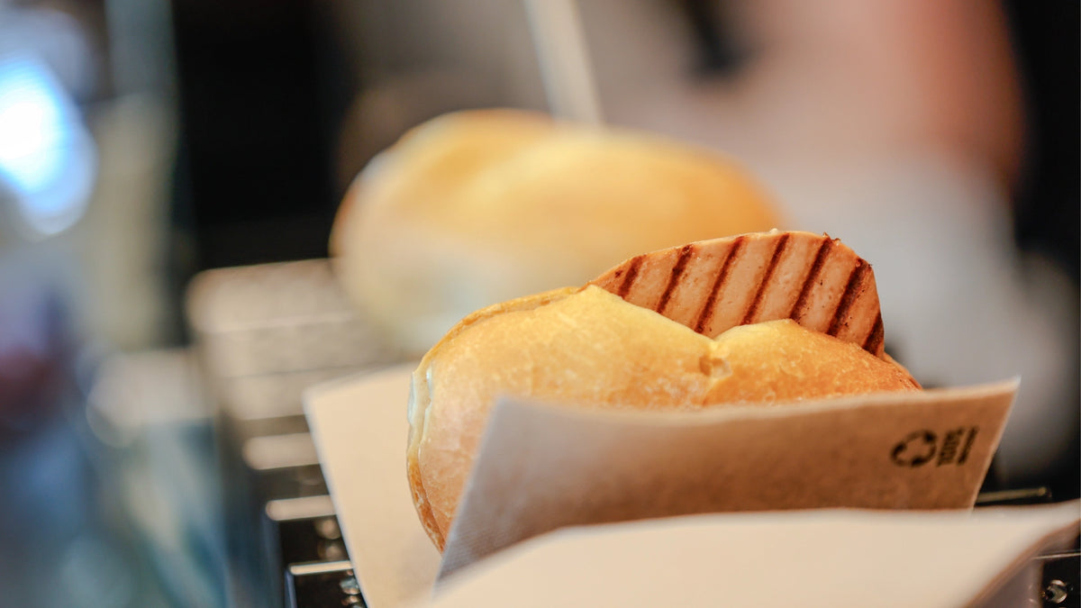 Brötchen mit gegrillter Scheibe veganem Leberkäse in einer Papierserviette an der Theke