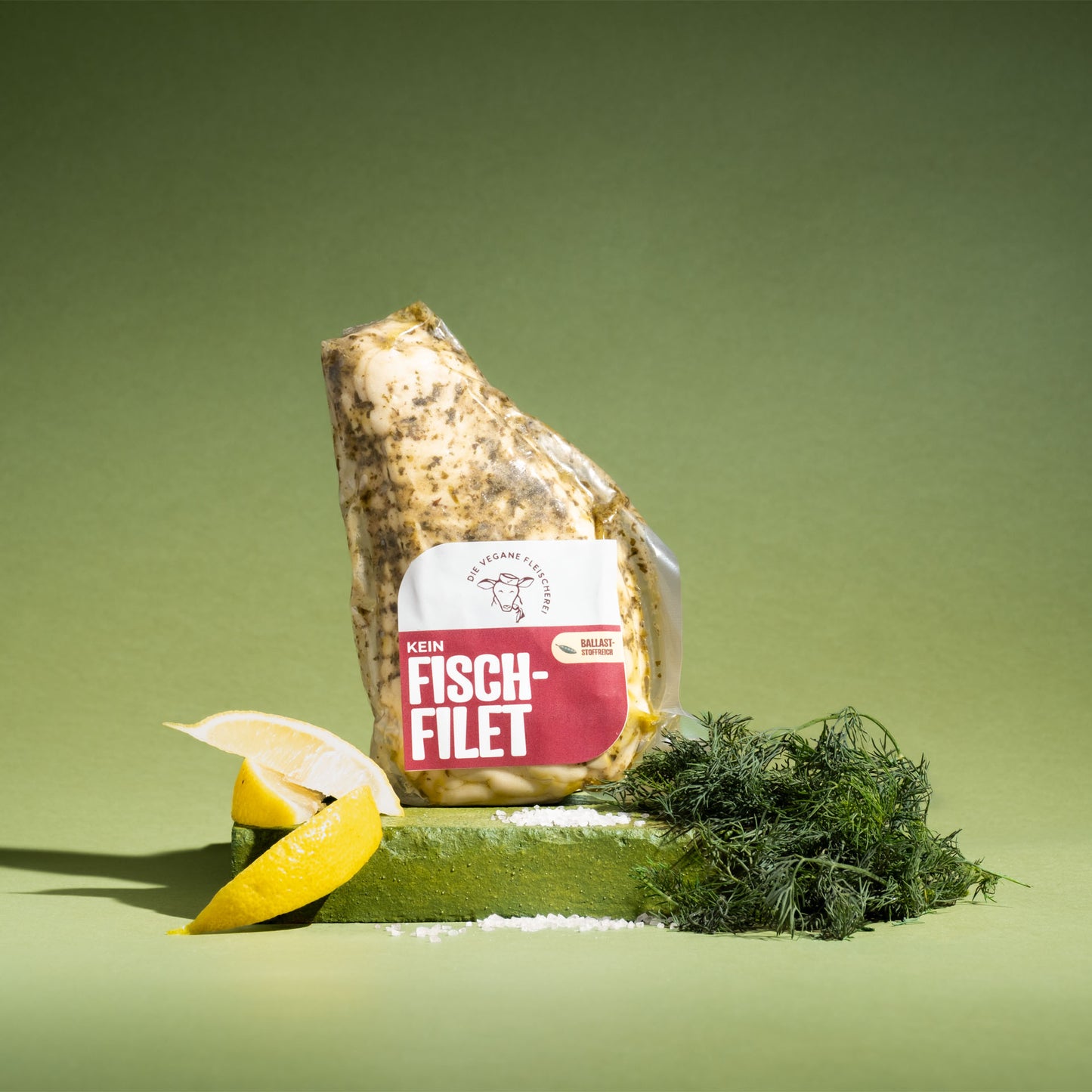 Veganes Fisch-Filet mit Zitrone und Dill, proteinreich und 100% pflanzlich, auf grünem Podest präsentiert