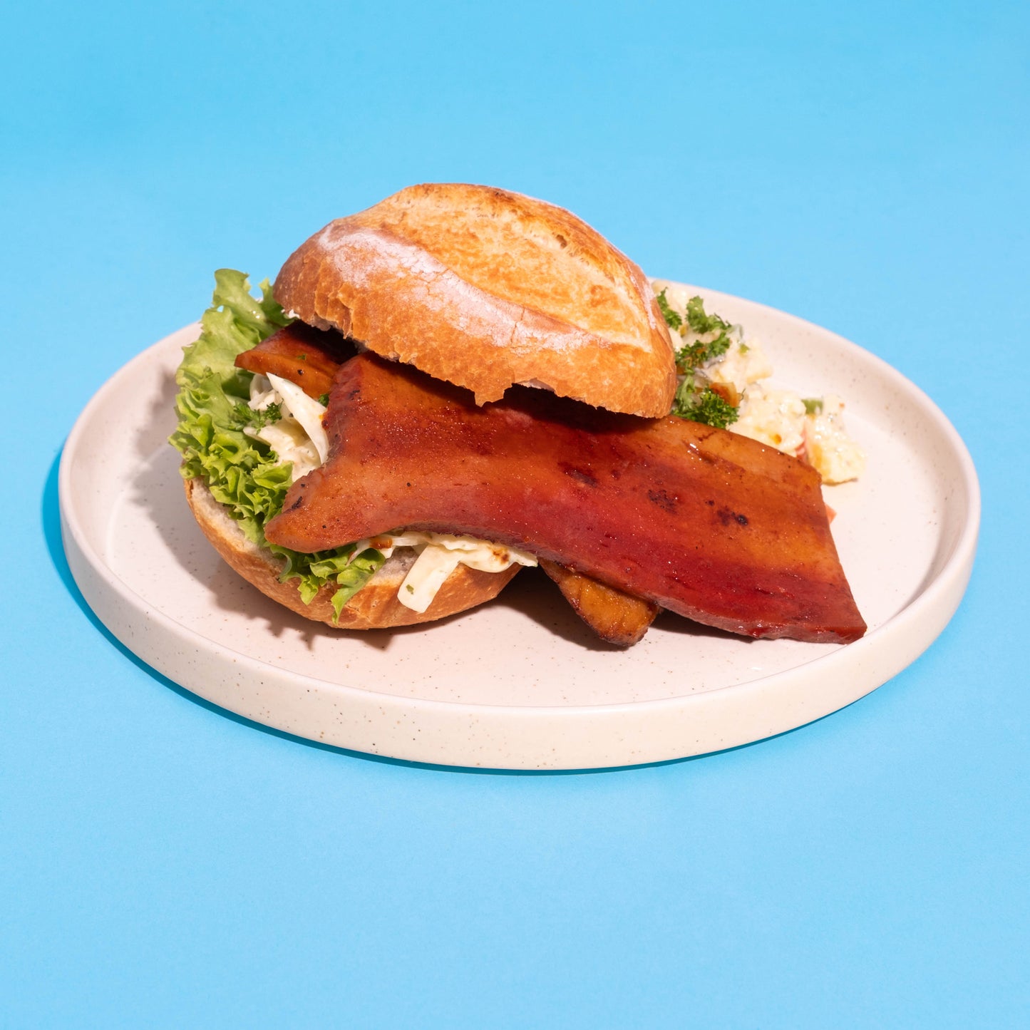 Veganer Grillbacon mit BBQ-Marinade im Brötchen und Kartoffelsalat.