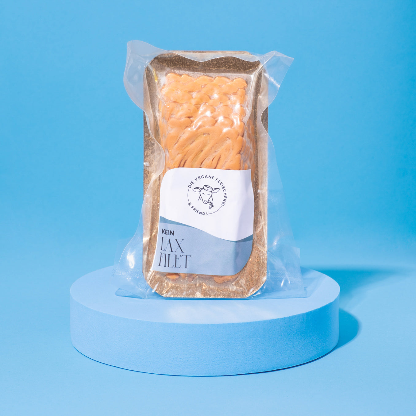 Veganes Laxfielt in Verpackung auf blauem Podest vor blauem Hintergrund.