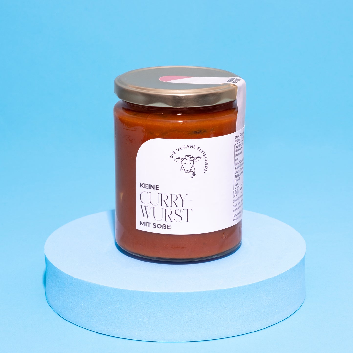Glas mit veganer Currywurst in Sauce auf blauem Podest vor blauem Hintergrund.