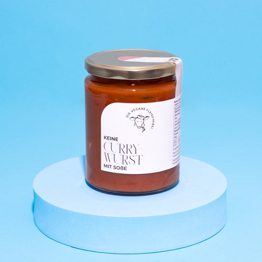 Glas mit veganer Currywurst in Sauce auf blauem Podest vor blauem Hintergrund.