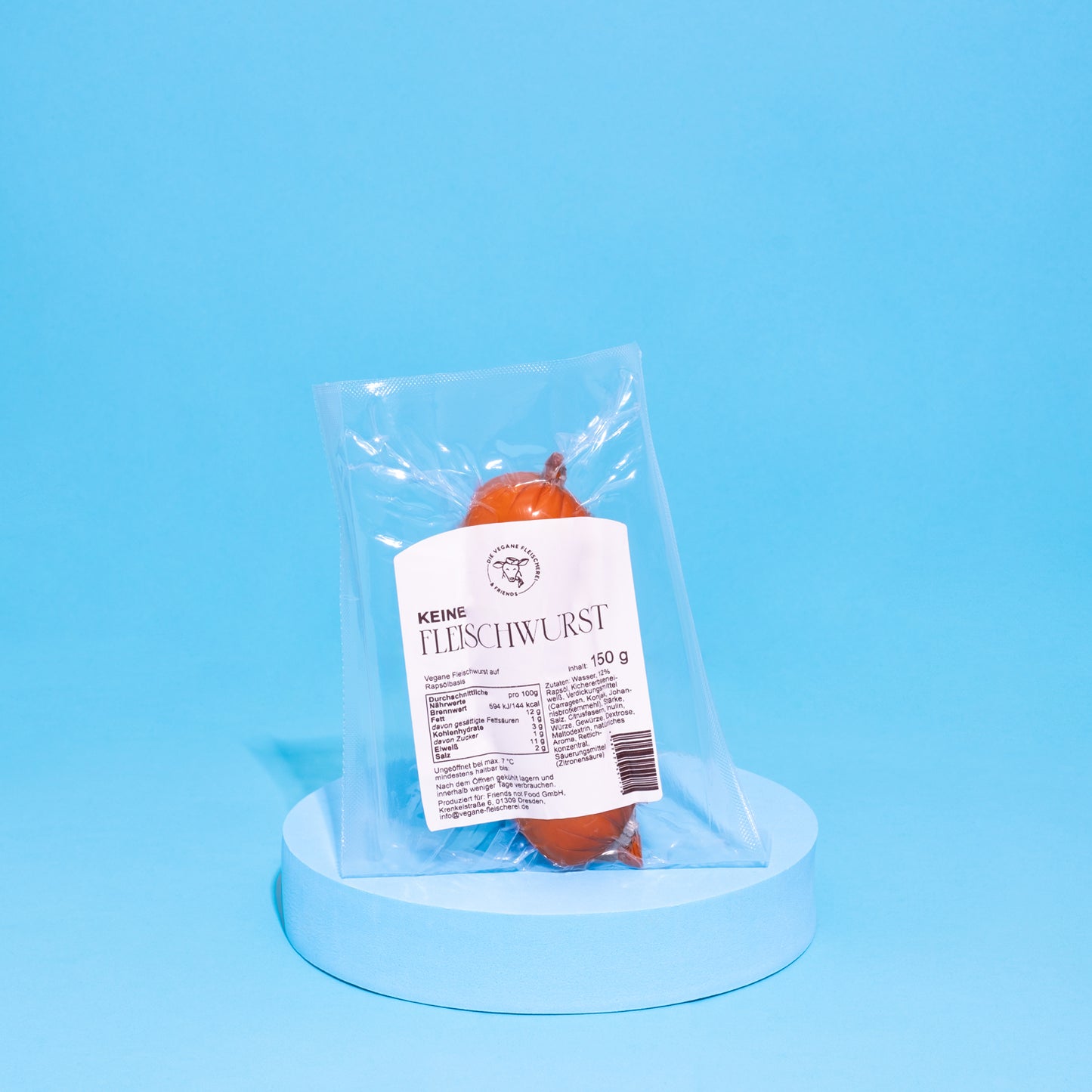 Vegane Fleischwurst auf blauem Podest vor blauem Hintergrund.
