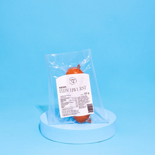Vegane Fleischwurst auf blauem Podest vor blauem Hintergrund.
