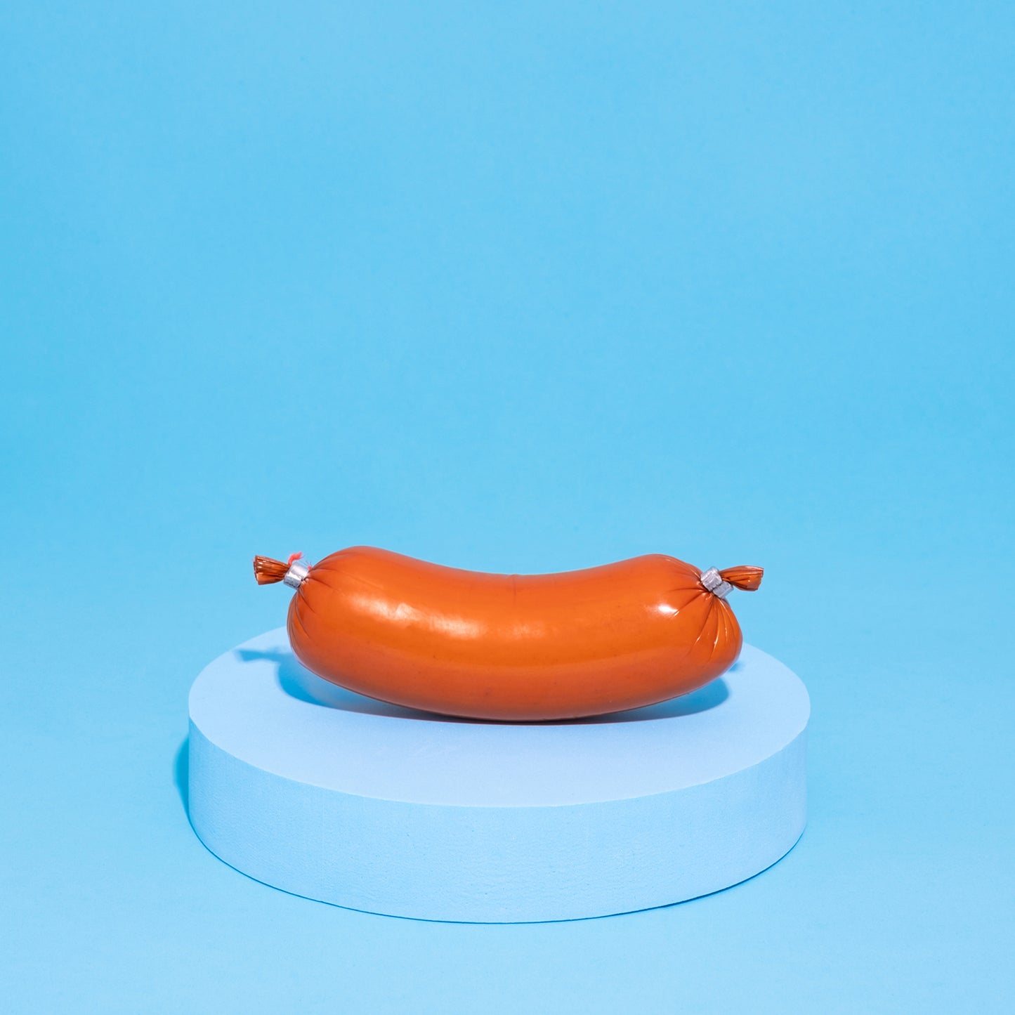 Vegane Fleischwurst auf blauen Podest vor blauem Hintergrund.