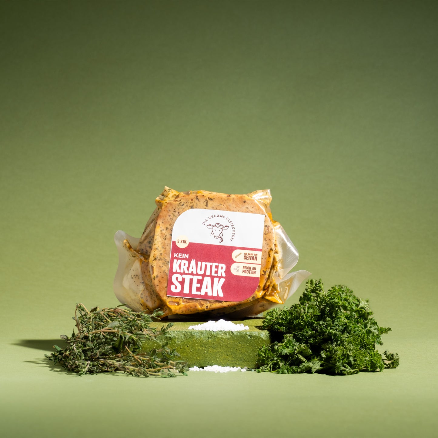 Vegane Kräutersteak-Paket auf grünem Podest mit frischen Kräutern, proteinreich und 100% pflanzlich