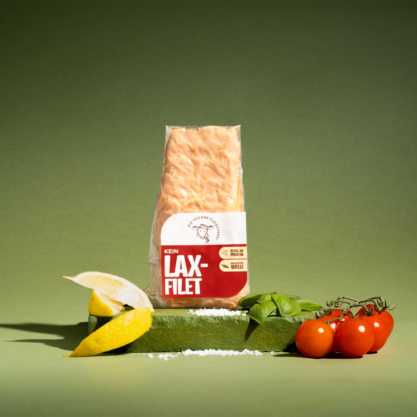 Veganes Lax-Filet, proteinreich & pflanzlich, mit Zitrone, Basilikum und Kirschtomaten auf grünem Podest