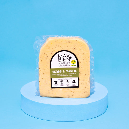 Veganer Kräuter-Knoblauch-Käse auf blauem Podest vor blauem Hintergrund.