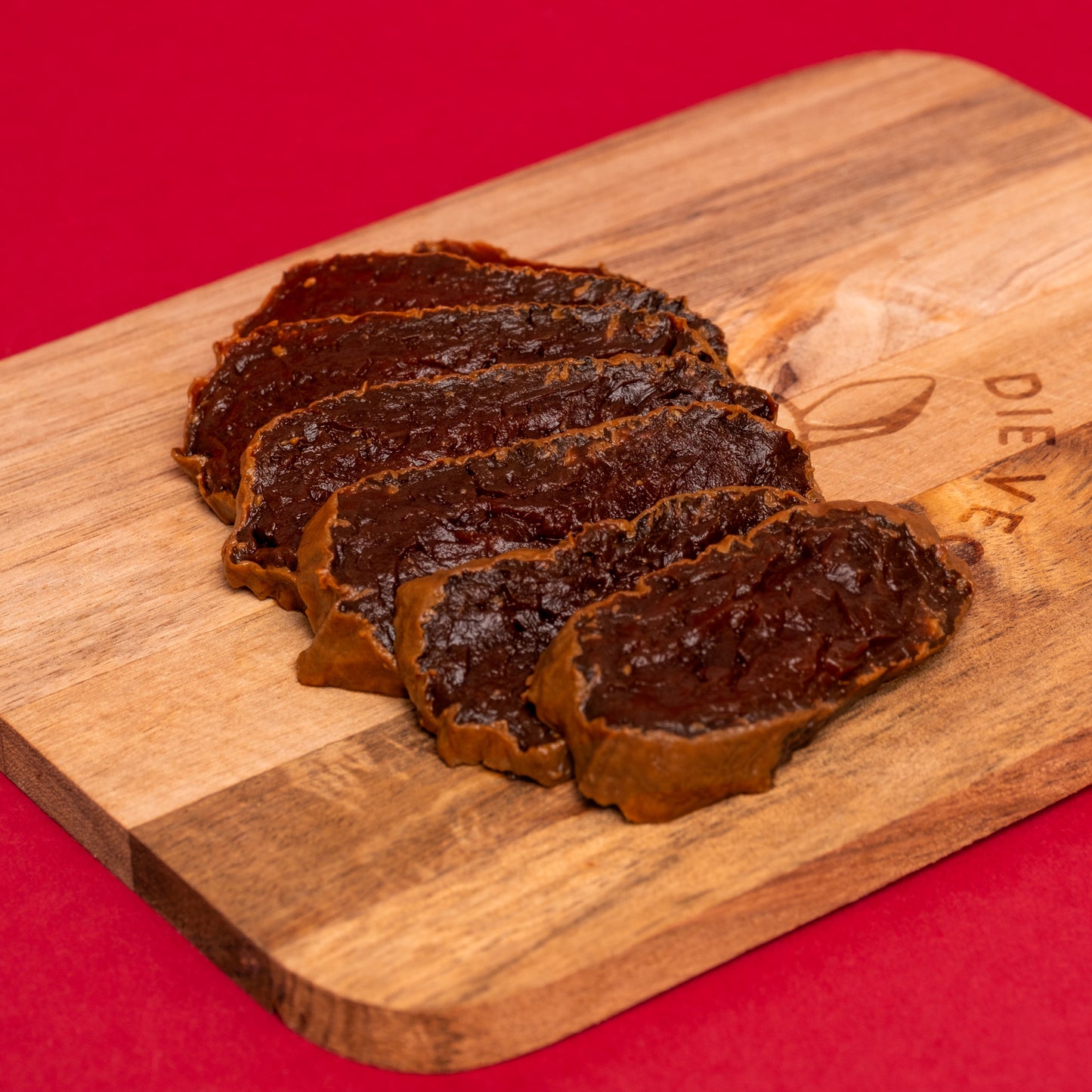 Aufgeschnittenes Rote-Bete-Schinken mit dunkelroter Farbe auf Holzbrett, roter Hintergrund.