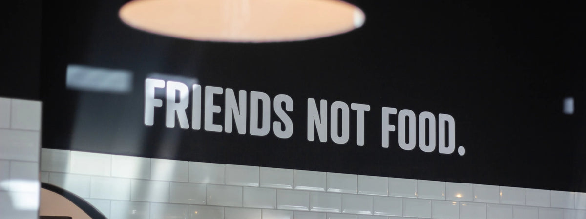 Weißer Schriftzug „Friends not Food.“ an einer dunklen Wand über weißen Fliesen
