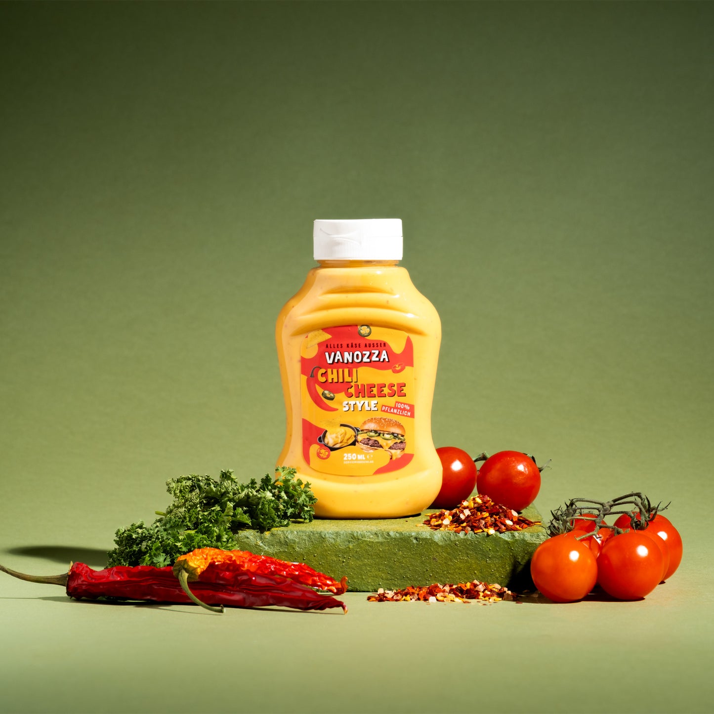 Vegane Chili Cheese Style Sauce in gelber Flasche mit frischen Tomaten, Chili und Petersilie, 100% pflanzlich