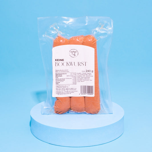 Verpackte vegane Bockwurst auf blauem Podest vor blauem Hintergrund.